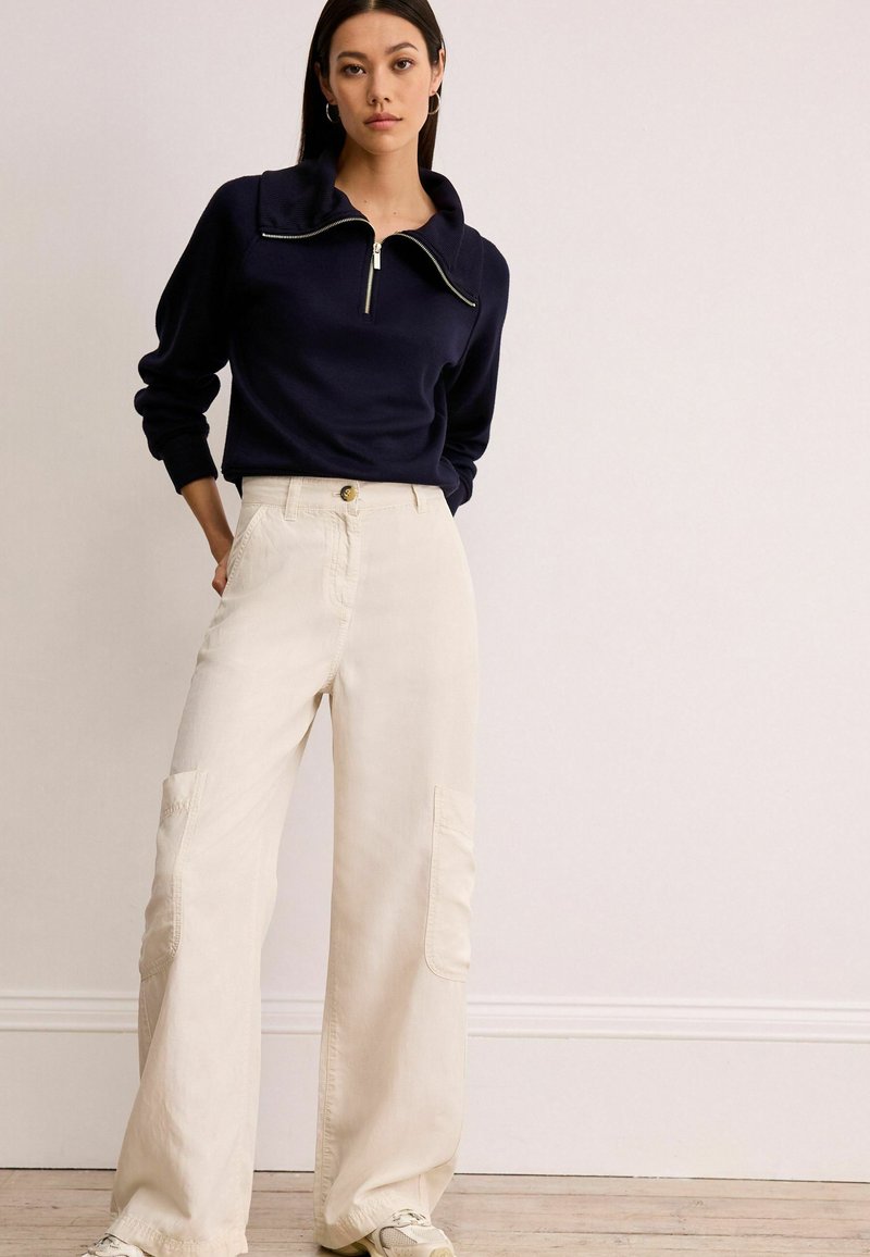 Navy Zip-up-Pullover mit hohem Kragen und gerippten Bündchen, kombiniert mit cremefarbenen, weiten Hosen mit Cargo-Taschen und einem Knopfverschluss vorne.