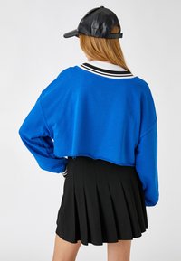Skórzany niebieski sweatshirt wykonany z miękkiego materiału, z czarno-białym paskiem u kołnierza. W połączeniu z plisowaną czarną spódnicą.