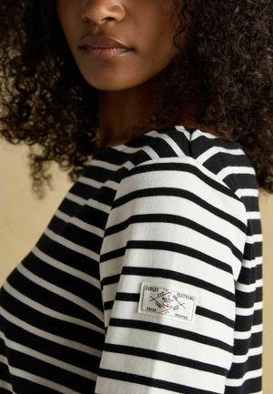 Black and white striped long-sleeve top with a textured fabric and a logo patch on the left sleeve. Close-up view of collar and shoulder.