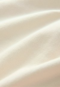 Tissu doux de couleur crème avec une texture côtelée fine et des plis délicats créant des vagues lisses.