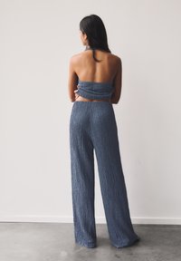 Blaues, strukturiertes Zweiteiler-Outfit mit einem trägerlosen Oberteil und weiten Hosen. Das Material zeigt ein zerknittertes Muster. Rückansicht angezeigt.