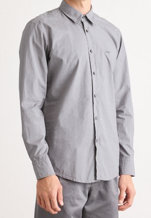 Man wearing a light gray long-sleeve button-up shirt with a collar and matching gray pants, standing against a plain background.