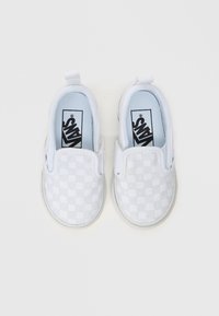 Fehér slip-on cipők sakktáblás mintával, vászonból készült, alacsony profilú dizájnnal és rugalmas oldalrészletekkel a kényelmes felhúzás érdekében.