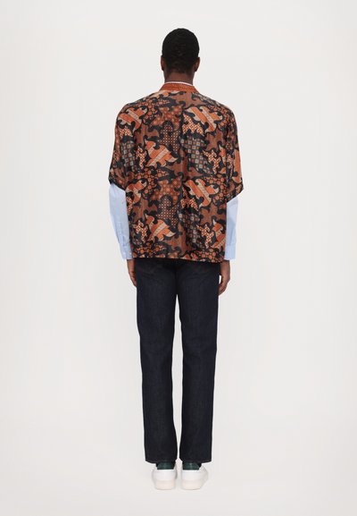 Korte mouw bedrukte shirt in donkere stof met oranje en blauwe ontwerpen, gecombineerd met donkere jeans en witte sneakers.