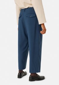 Blauwe geplooide broek met een getailleerde pasvorm, met twee achterzakken met knoopsluitingen, gemaakt van een textuurstof.
