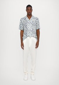 Korte mouwen shirt in lichtblauw met een bloemenpatroon, gecombineerd met witte linnen broek en witte sneakers. Zachte stof en een ontspannen pasvorm.