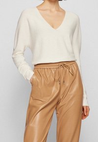 Pull en maille crème avec col en V et manches longues, associé à un pantalon de jogging beige en faux cuir, doté d'une taille à cordon de serrage et de poches latérales.