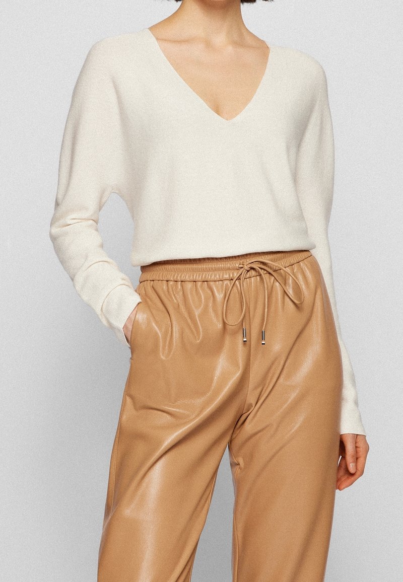 Pull en maille crème avec col en V et manches longues, associé à un pantalon de jogging beige en faux cuir, doté d'une taille à cordon de serrage et de poches latérales.
