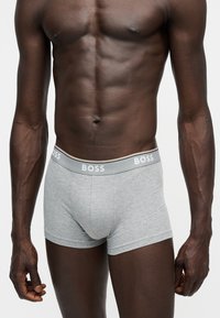 Buste masculin portant un boxer gris clair avec une ceinture grise marquée BOSS, sur un fond blanc uni.