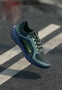 Nike running shoe in shades of teal and gray, with mesh panels, reflective accents, and textured sole. Features laces and logo.