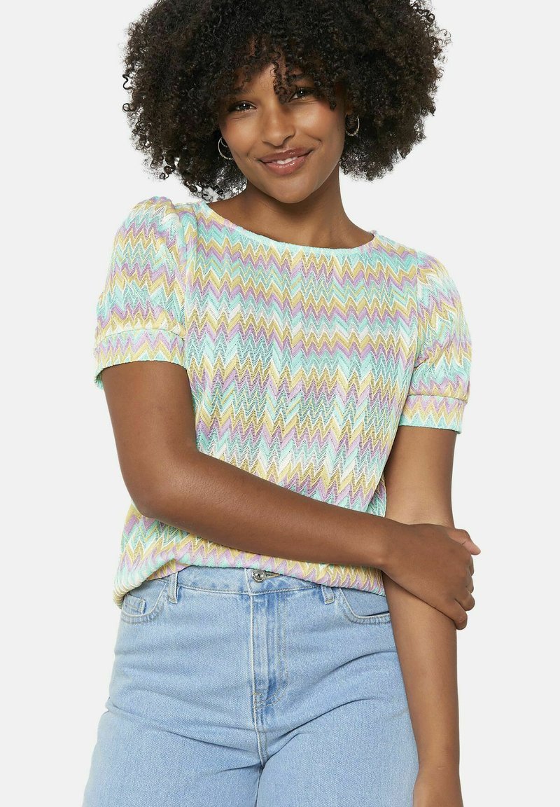Top a maglia con motivo zigzag in colori pastello, scollo rotondo e maniche corte a palloncino. Indossato con jeans leggeri a vita alta di colore blu.