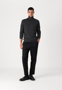 Maglione a collo alto grigio scuro con un logo sottile, abbinato a pantaloni neri e scarpe nere. Design semplice e lineare con una texture liscia.