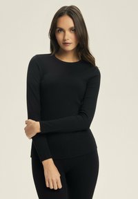 Czarny, dopasowany, długi rękaw top z prążkowanej tkaniny, z okrągłym dekoltem i gładką teksturą, zestawiony z dopasowanymi czarnymi spodami.