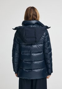 Veste matelassée marine avec col montant et capuche intégrée. Présente des sections matelassées et une texture lisse et brillante.