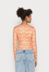 Camisola laranja de manga longa com um padrão texturizado. O tecido é semi-transparente e é modelada com um decote arredondado e uma forma ajustada.