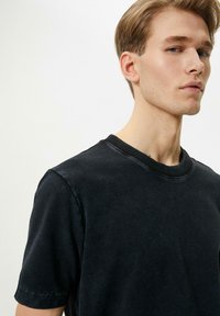 Camiseta negra de manga corta con un acabado texturizado y cuello acanalado. La camiseta tiene un ajuste relajado y sutiles reflejos de luz.