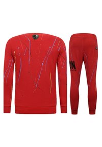 Rode katoenen trainingsoutfit met een sweatshirt met ronde hals en tapered broeken. Het ontwerp bevat spetterpatronen in blauw, geel en zwart.