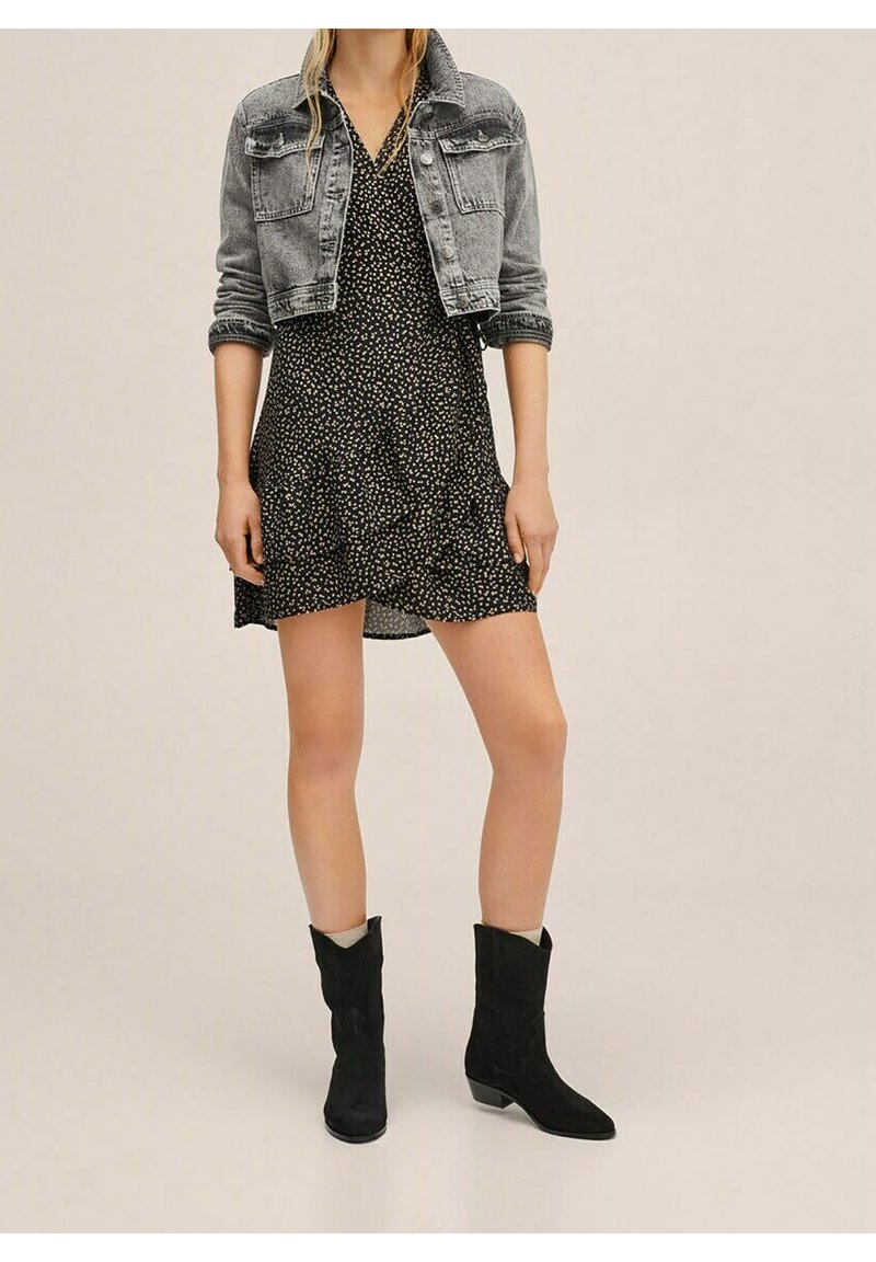Černé krátké šaty s bílým květinovým vzorem, se zpevněným lemem, kombinované se šedou džínovou bundou a černými semišovými kotníkovými botami.