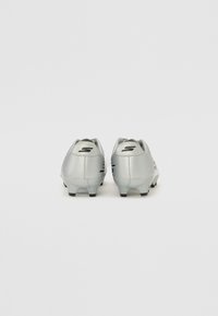 Des chaussures de football grises avec une tige lisse, un talon arrondi et des accents noirs. Équipées de crampons moulés pour une traction sur les surfaces en herbe.