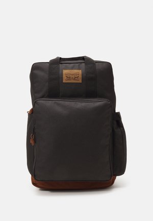 Zaino rettangolare nero con tasca frontale con zip, tasche laterali, manici superiori, base in suede marrone e patch con logo in pelle color cuoio.
