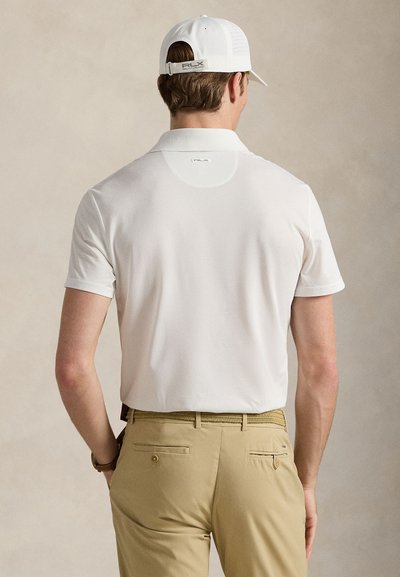 Λευκό πόλο πουκάμισο με κοντά μανίκια, με γιακά και λογότυπο στο πίσω μέρος. Συνδυάζεται με χακί παντελόνι, που διαθέτει ζώνη με υφαντή υφή.