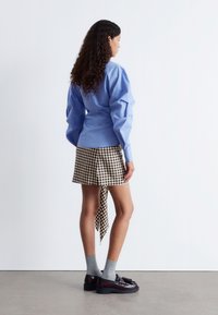 Light blue puff-sleeve shirt, brown and white gingham mini skirt with a side tie, gray socks, and black platform loafers.