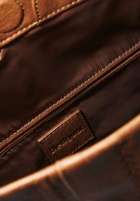 Braune Lederhandtasche mit genähtem Innenfutter, sichtbarem Reißverschluss und einem Lederlabels mit der Aufschrift "Desigual."