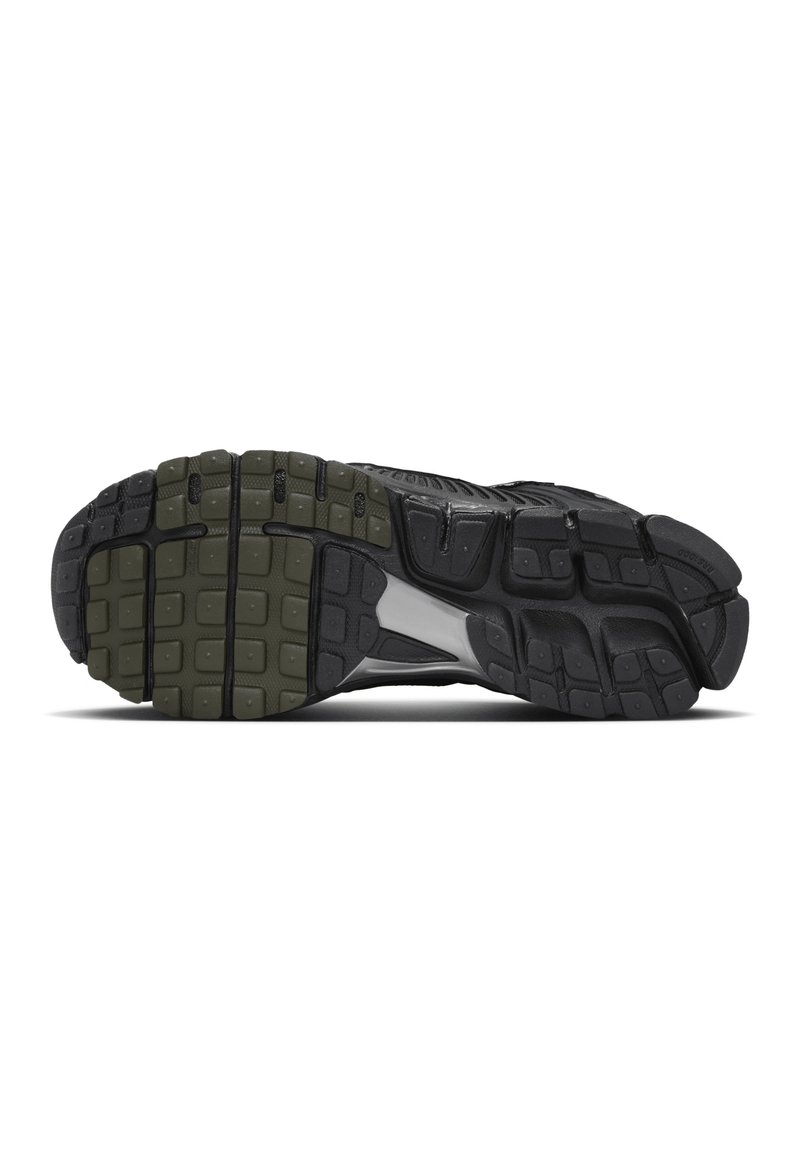 Semelle en caoutchouc de chaussure de sport noire avec un motif texturé. Comprend un matériau en caoutchouc, des rainures flexibles et un accent vert. Design antidérapant.