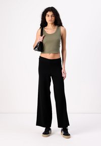 Olivově zelený žebrovaný crop top s kulatým výstřihem, kombinovaný s černými kalhotami s širokými nohavicemi. Doplněno malou černou kabelkou a černými teniskami.