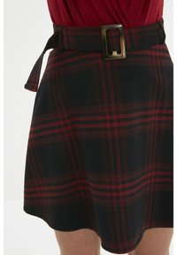 Jupe à carreaux noir et rouge avec une ceinture assortie et une boucle rectangulaire, port�ée avec un haut rouge, montrée de la taille à mi-cuisse.