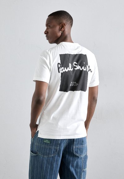 Bijela pamučna majica s crnim pravokutnim grafičkim uzorkom na leđima na kojem je u bijelom rukopisom ispisano "Paul Smith" i dodatni tekst ispod.
