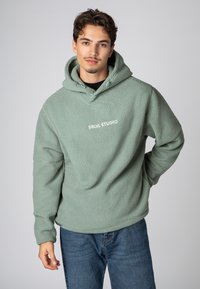 Fleece hoodie in gedempt groen met een gestructureerd oppervlak. Beschikt over een capuchon met trekkoord en een wit "SBLVL STUDIO" logo op de borst.