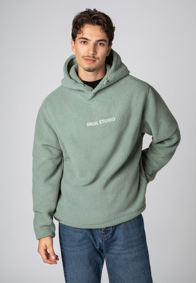 Fleece hoodie in gedempt groen met een gestructureerd oppervlak. Beschikt over een capuchon met trekkoord en een wit "SBLVL STUDIO" logo op de borst.