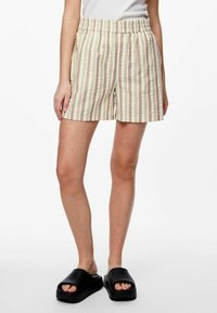 Pantaloni corti a righe beige e bianchi con vita elasticizzata e tasche laterali, realizzati in tessuto leggero, abbinati a sandali neri a infradito.