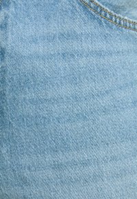 Ljusblå denimtyg med en slät yta och ett subtilt vävt mönster. Synliga sömmar längs kanterna.