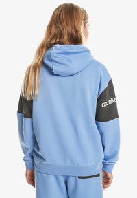 Sweatshirt à capuche bleu avec des panneaux d'accent noir sur les manches. Le matériau semble doux avec une coupe décontractée et des poignets et une taille côtelés.