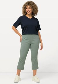 T-shirt bleu marine raccourci avec un col en V, associé à un pantalon vert clair arrivant aux chevilles. La mannequin porte des baskets blanches et de grandes boucles d'oreilles.