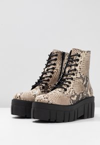 Stivali ankle stringati con motivo in pelle di pitone finta, in toni beige e marrone, con una spessa suola piattaforma nera e cerniera laterale.
