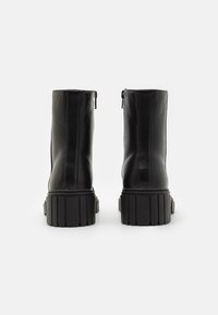 Bottines en cuir noir avec une finition lisse, dotées d'une semelle épaisse et striée ainsi que d'une fermeture éclair sur le côté.