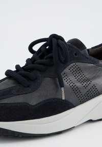 Baskets bleu marine avec une combinaison de matériaux lisses et texturés. Présente des détails perforés, des lacets plats et une semelle blanche.