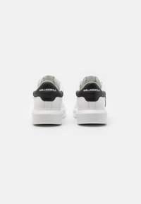 Sneaker bianche in pelle con una suola spessa, dotate di un tassello sul tallone nero con il marchio "KARL LAGERFELD" e un design semplice e minimalista.
