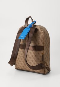 Sac à dos texturé marron avec un motif de logo sur toute la surface, des bretelles marron et une touche de bleu sur l'étiquette. Il dispose d'une poche zippée et d'une conception robuste.
