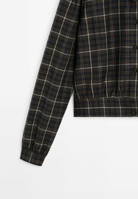 Manche longue d'une chemise à carreaux marron foncé avec des fines lignes blanches et beiges, poignet boutonné et boutons noirs à l'avant.