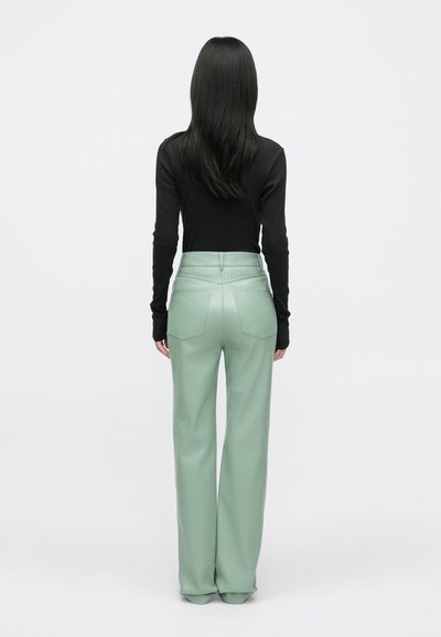 Mėtų žalia plačių kojų kelnių su didele liemeniu, lygia tekstūra ir dviem užpakalinėmis kišenėmis, pavaizduotų iš nugaros, derinamos su juoda ilgomis rankovėmis palaidine.
