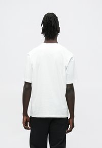 Biele bavlnené tričko s krátkymi rukávmi a okrúhlym výstrihom, s hladkou textúrou a voľným strihom, zobrazené zozadu.