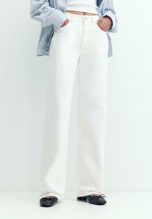 Białe spodnie z szerokimi nogawkami i wysokim stanem, noszone z czarnymi balerinami, w połączeniu z krótkim białym topem i niebieską koszulą w kratę, z rękami w kieszeniach.