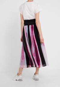 Maxikjol med livliga vertikala ränder i rosa, lila och svart. Har en enfärgad svart midja och mjuk, flödande tyg.