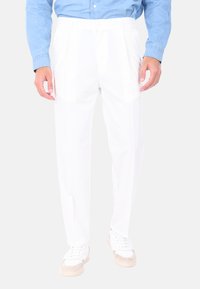 Pantaloni bianchi con design a gamba dritta, realizzati in un tessuto leggero. Presentano una parte frontale piatta, tasche laterali e sono abbinati a sneakers bianche.