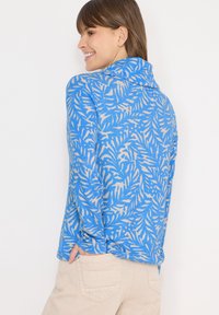 Haut bleu à manches longues avec un motif de feuilles en beige clair. Présente un col montant et une coupe décontractée, confectionné dans un tissu doux et texturé.