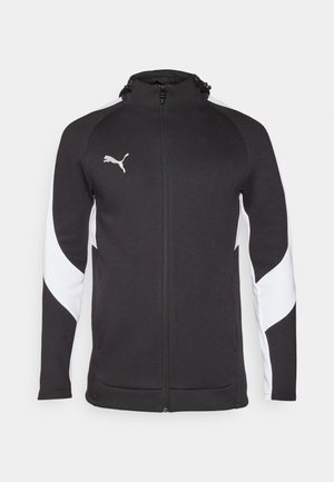 Fekete sportdzseki fehér oldalsó panelek nélkül, teljes zipzárral, magas gallérral és egy kis ezüst logóval a mellkasán. Texturált anyagból készült.